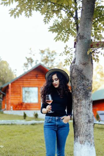 a woman standing next to a tree holding a glass of wine at Complex turistic Traisteni din Valea Doftanei in Podu lui Neag