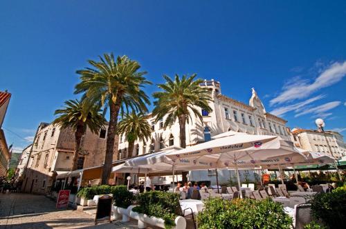 a patio with umbrellas and palm trees in front of a building at Hotel Sveti Kriz in Trogir