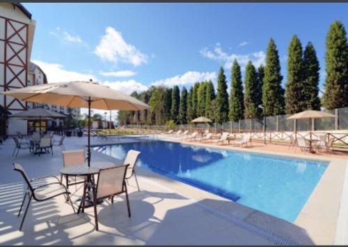 uma piscina com mesas e cadeiras e um guarda-sol em SUÍTE EM PEDRA AZUL - Condomínio VISTA AZUL em Domingos Martins