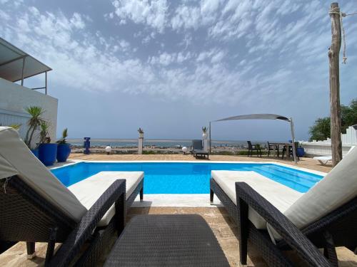 - une piscine avec 2 chaises longues et l'océan dans l'établissement LES OLIVIERS, à Oualidia