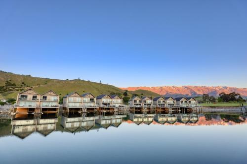 a row of houses on the water with mountains in the background at Marsden Lake Resort Central Otago in Cromwell