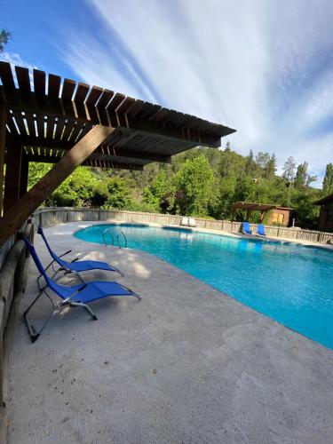 a pool with two blue chairs and a wooden pergola at Tumuñan Lodge in El Llano