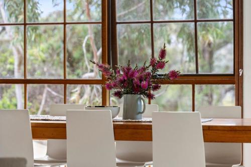 a table with white chairs and a vase with flowers at Yirrip House Nestled on the edge of National Park in Aireys Inlet