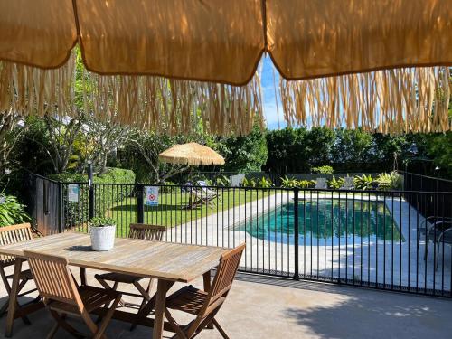 a wooden table with chairs and an umbrella and a pool at The Arabella North Coast in Wollongbar