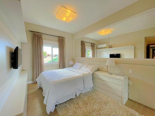 1 dormitorio con cama blanca y espejo en Apartamento ha 3 minutos da Rua Coberta - Gramado, en Gramado