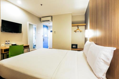 1 dormitorio con 1 cama blanca grande y escritorio en Hotel Citradream Tugu Yogyakarta, en Yogyakarta