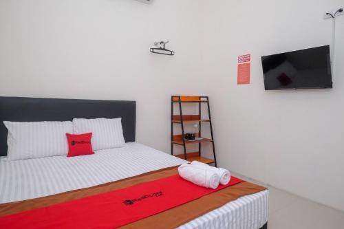 RedDoorz near Alun Alun Magelang 2 في ماغيلانغْ: غرفة نوم بسرير وبطانية حمراء وتلفزيون بشاشة مسطحة