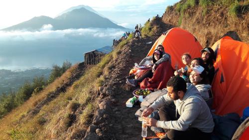 a group of people sitting on a hill with tents at Mount Batur Camping Ground with Natural Hot Spring in Kintamani