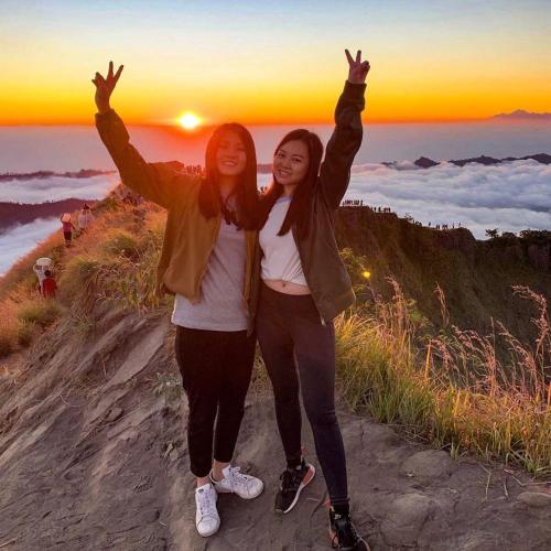 two girls standing on a hill with their hands in the air at Mount Batur Camping Ground with Natural Hot Spring in Kintamani