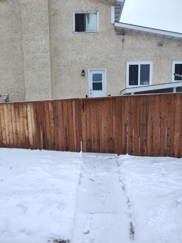 a wooden fence with snow in front of a house at Tranquil & Tasteful One Bdrm Private Suite NE in Edmonton