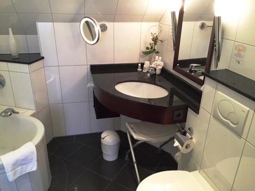 ein Badezimmer mit einem Waschbecken, einem WC und einem Spiegel in der Unterkunft Akzent Hotel Höltje in Verden
