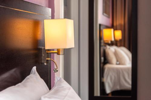a lamp on a wall next to a bed with pillows at Hôtel Le Mondon Metz in Metz