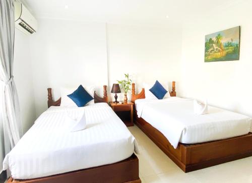 two beds in a room with white sheets and blue pillows at The Blanc Residence in Siem Reap
