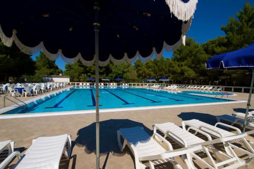 a swimming pool with white chairs and an umbrella at Hotel Portonuovo in Vieste