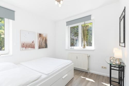 ein weißes Schlafzimmer mit einem Bett und Fenstern in der Unterkunft Ferienwohnung Die 2b in Timmendorfer Strand