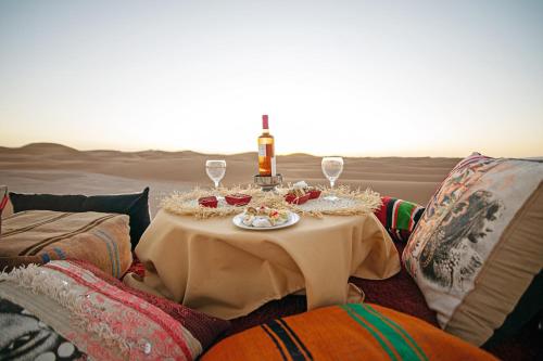 a table in the middle of the desert with a bottle and glasses at Ghazala Camp - Luxury Erg Chigaga Magic in Mhamid