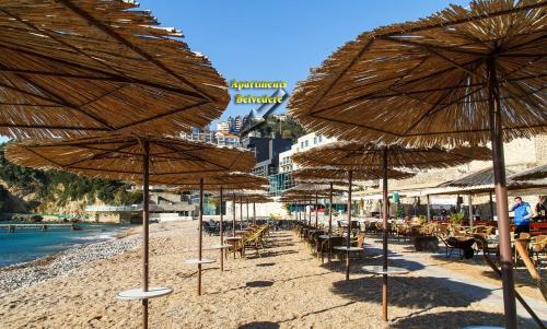 a beach with many straw umbrellas and tables and chairs at Belvedere Apartments in Budva