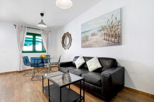 a living room with a black leather couch and a table at Mar de Lava Sunrise Fuerteventura in Pozo Negro