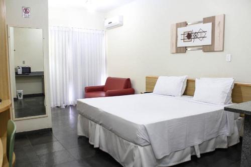 1 dormitorio con 1 cama blanca y 1 silla roja en Bravo Suites São Carlos, en São Carlos