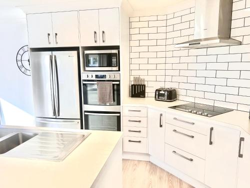 uma cozinha branca com armários e electrodomésticos brancos em Home In On Family - 230m from Papamoa Beach em Papamoa