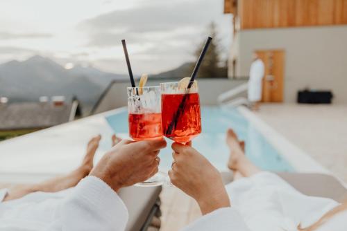 a person holding two drinks with their hands at Hideaway Hotel Montestyria Chalets & Suiten in Mariazell