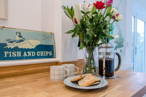 a table with a vase of flowers and a plate of cookies at 21 Park Lane, Aldeburgh in Aldeburgh