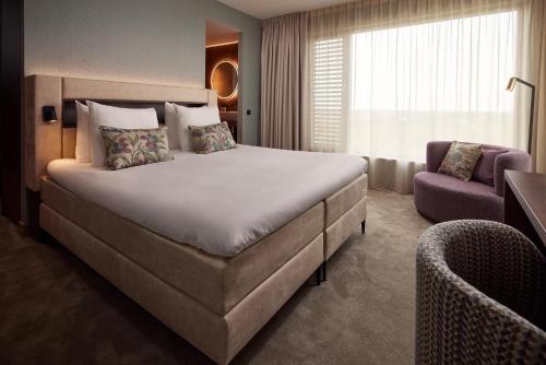 Van der Valk Hotel Lelystad في ليليستاد: غرفة فندقية بسرير كبير وكرسي