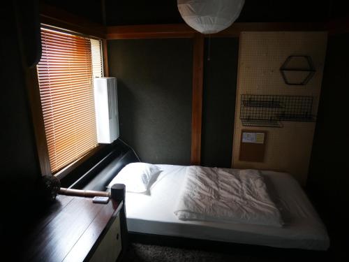 1 dormitorio con 1 cama blanca y ventana en 駅前宿舎 禪 shared house zen, en Eiheiji