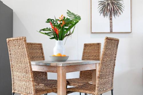 a dining room table with two chairs and a vase with flowers at 'Botanica Aguila' Chic Nightcliff Balcony Pad in Darwin