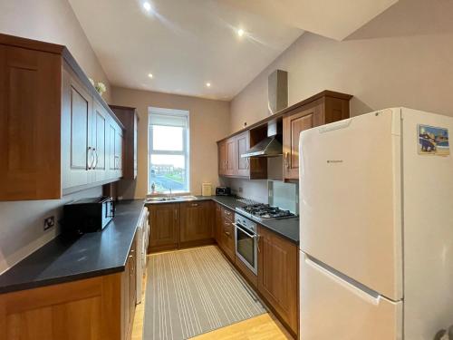 a kitchen with wooden cabinets and a white refrigerator at The Beach Front Apartment, Amazing Frontline Sea Views in Tynemouth