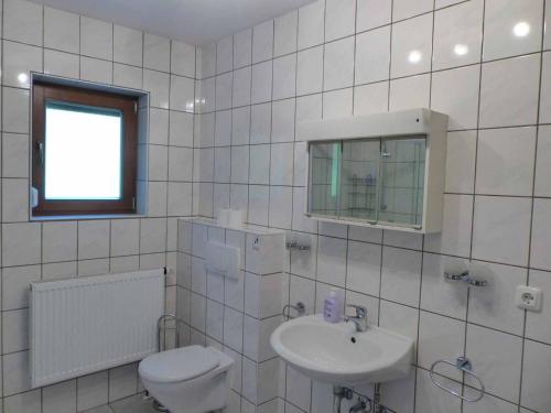 a white tiled bathroom with a toilet and a sink at FeWo H.Reußwig in Arrach