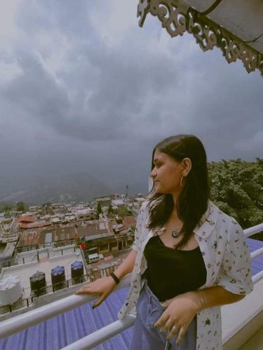a woman standing on a balcony overlooking a city at Swastika Homestay and Travels Kurseong Bazar Near HDFC Bank NH55 Road Kurseong in Kurseong