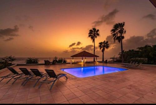 Willibrordus的住宿－Ocean Front VillaDelMar-Beach Access-Private Pool-10 Guests-，一个带椅子的游泳池,享有日落美景
