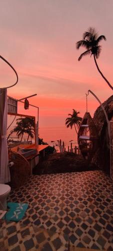 einen Sonnenuntergang über einem Strand mit Palmen und dem Meer in der Unterkunft Obrigado by Craftels in Cabo de Rama