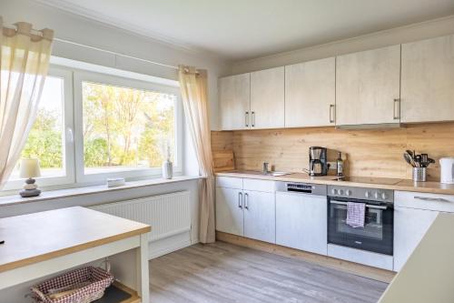 eine Küche mit weißen Schränken, einem Tisch und einem Fenster in der Unterkunft Ferienhaus Tidenkieker in Nordstrand