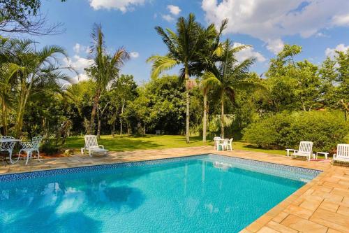 a swimming pool with chairs and a table and trees at LINDA CHACARA EM CONDOM 30 MIN DE SP piscina climatizada, churrasqueira, wifi, 5 quartos, amplo jardim in Cajamar