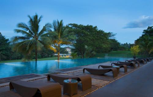 a resort swimming pool with chairs and palm trees at Novotel Manado Golf Resort & Convention Center in Manado