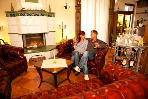 a man and woman sitting in a living room with a fireplace at Jagdschloss Waldsee in Waldsee