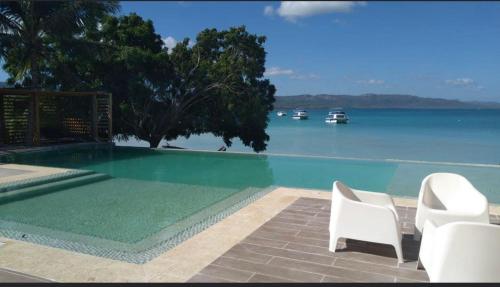 a swimming pool with two white chairs and the water at Hotel Sand Bay in Punta Rucia