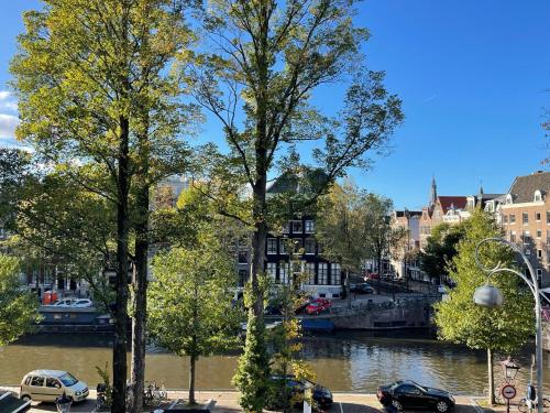 a river with cars parked next to trees and buildings at Little Tulip in Amsterdam