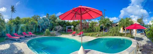 a swimming pool with a red umbrella and chairs and a pool at Xainã Pousada de Charme in Cumbuco