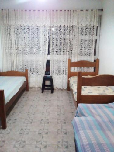 a bedroom with two beds and a window with curtains at Kitinete em Itanhaem in Itanhaém