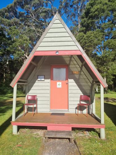 a small house with two chairs and a red door at Strahan Retreat Holiday Park in Strahan
