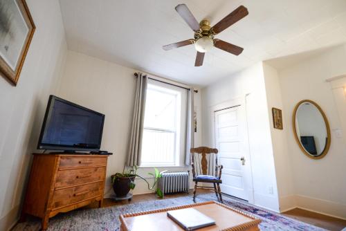 a living room with a ceiling fan and a tv at Brown & Hawkins Historical Apartments in Seward