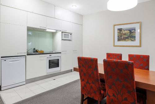 a kitchen with a wooden table and red chairs at Adina Citylife Wellington in Wellington