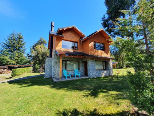 a wooden house on a grassy yard with two blue chairs at Encanto del Rio in Villa La Angostura