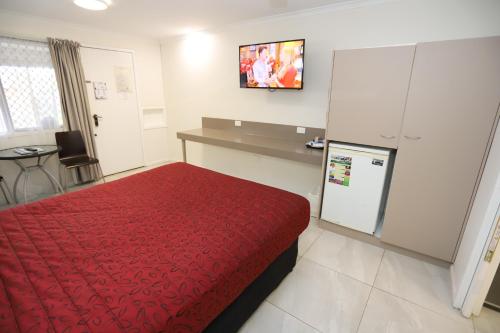 Habitación de hotel con cama roja y TV. en Miners Lodge Motor Inn, en Mackay