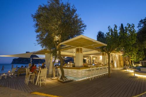 a restaurant with tables and chairs on a deck near the water at Akrotiri Beach Resort Hotel - Adult Friendly in Paleokastritsa