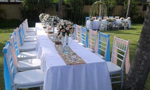 a long table with white tables and chairs with flowers at Villa Samudra Luxury Beachfront in Ketewel