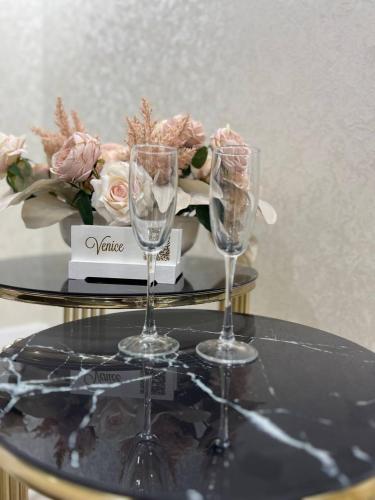 zwei Weingläser auf einem Tisch mit einem Blumenstrauß in der Unterkunft Grand SPA Hotel in Qostanai